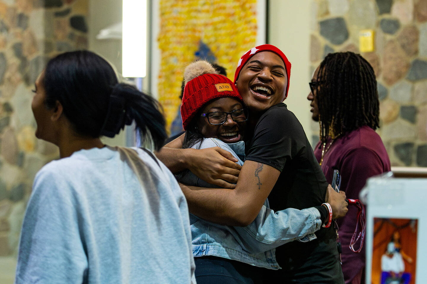 Two individuals embrace warmly in a joyful hug, their laughter echoing in a brightly lit indoor space.